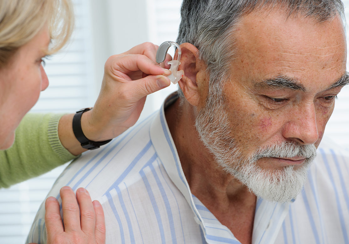 Hearing Aid Doctor inserting hearing aid in senior's ear